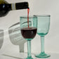 Red wine being poured into two green wine glasses on a white background