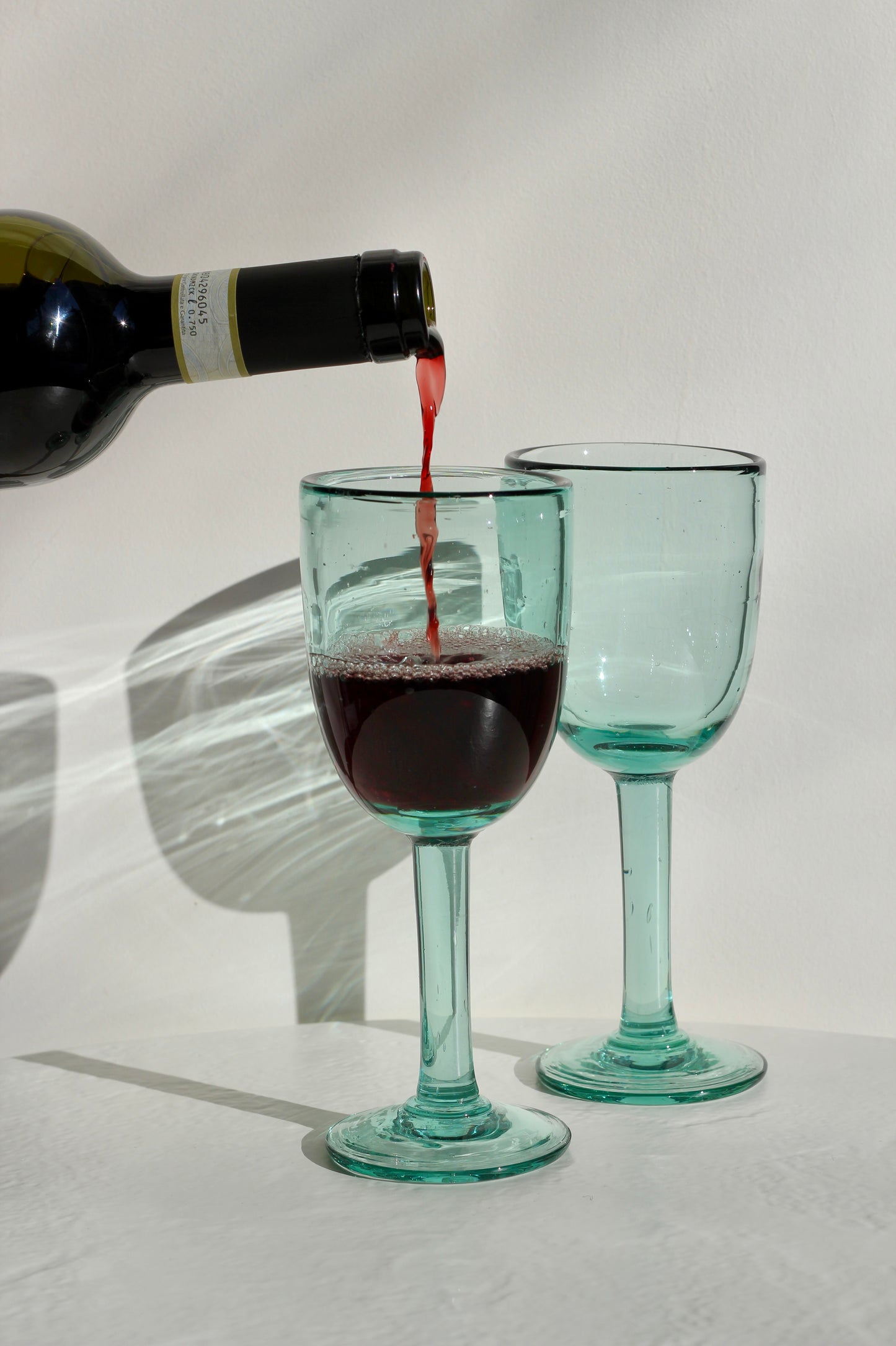 Red wine being poured into two green wine glasses on a white background