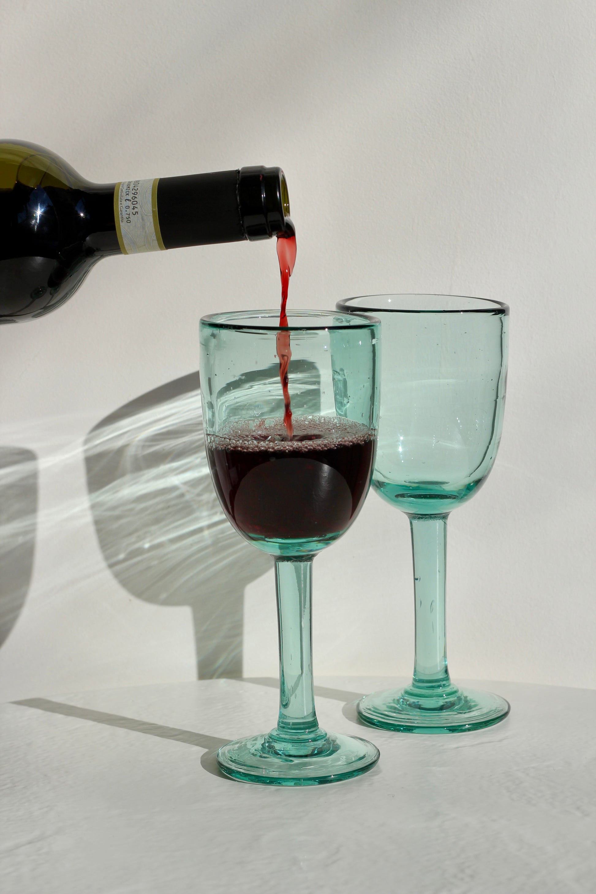 Red wine being poured into two green wine glasses on a white background