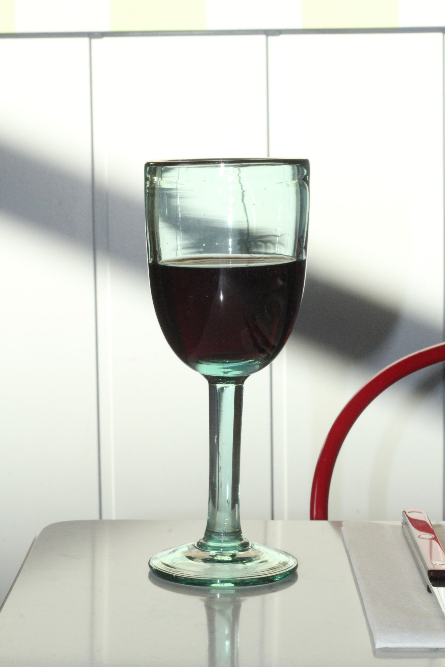 Handblown recycled wine glass on a reflective surface with a lamp in the background