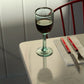 Handblown recycled glass of red wine on a table with cutlery and a red chair in the background