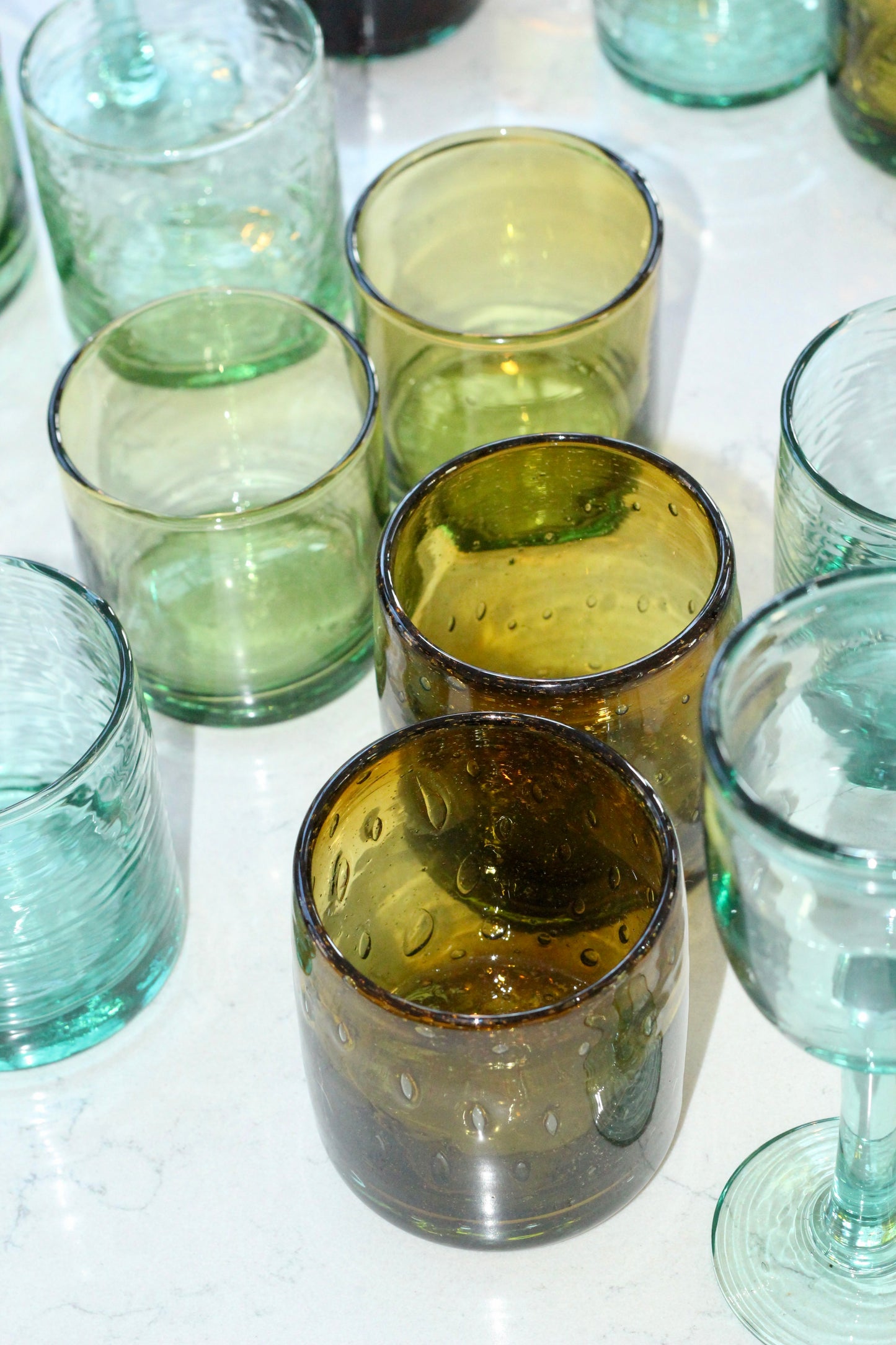 Collection of green and clear handblown glass tumblers on a white surface