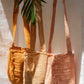 Three woven handbags in different colors hanging against a white wall.