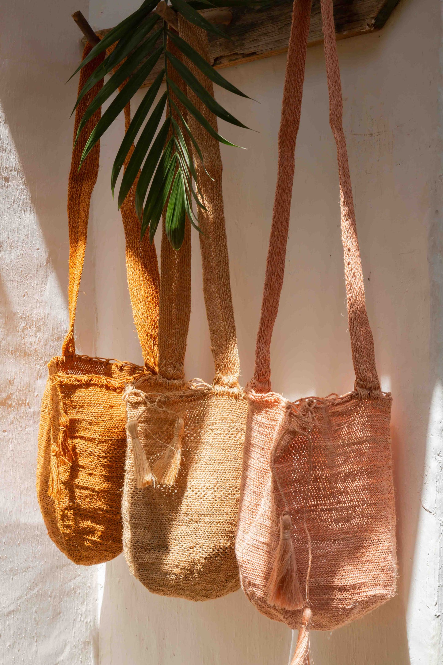 Three woven handbags in different colors hanging against a white wall.