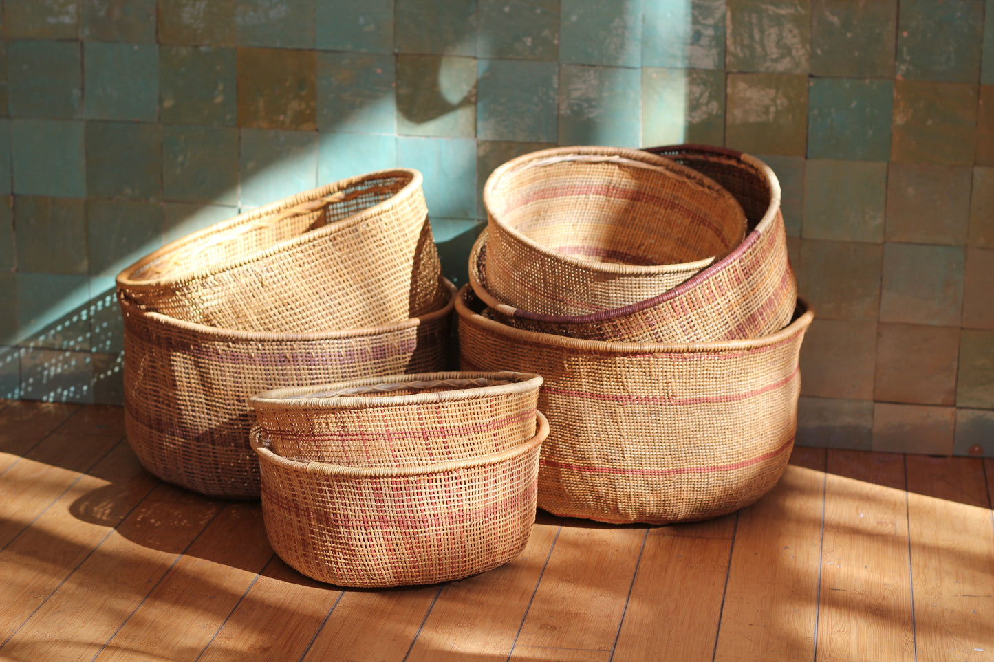 Set of handwoven baskets on a wooden floor with a tiled wall background