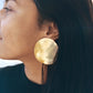 Close-up of a person wearing a large gold hand-hammered earring with a neutral background
