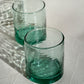 Two wavy green glass tumblers on a textured white surface