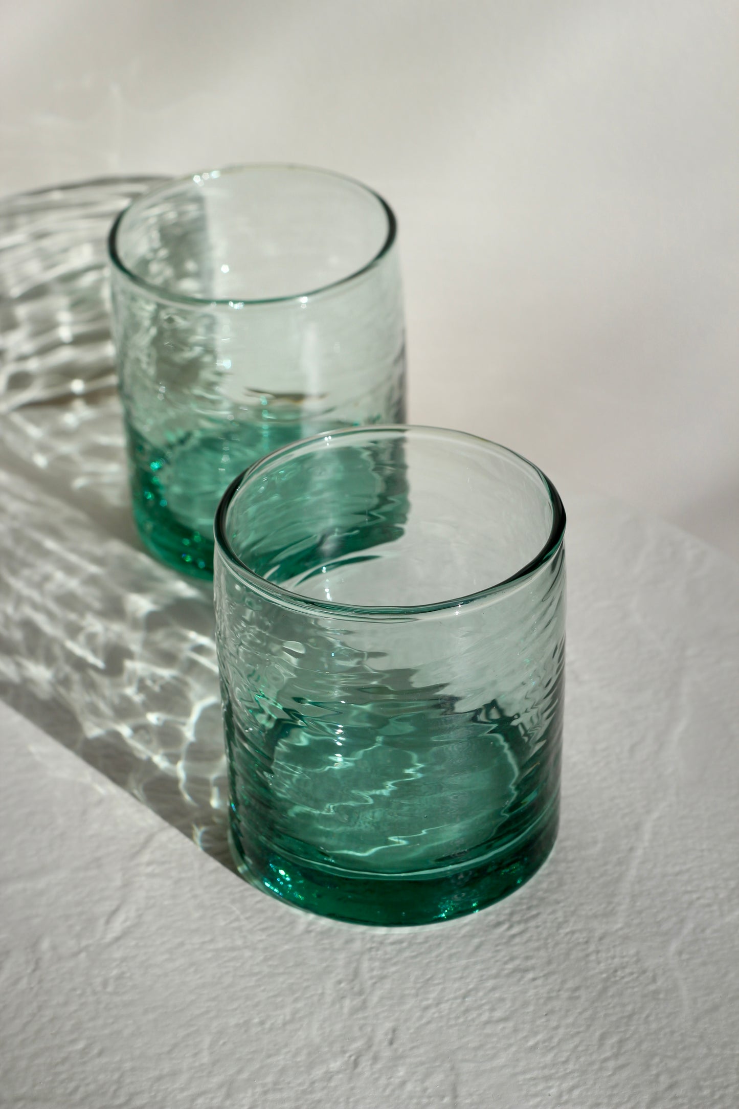 Two wavy green glass tumblers on a textured white surface