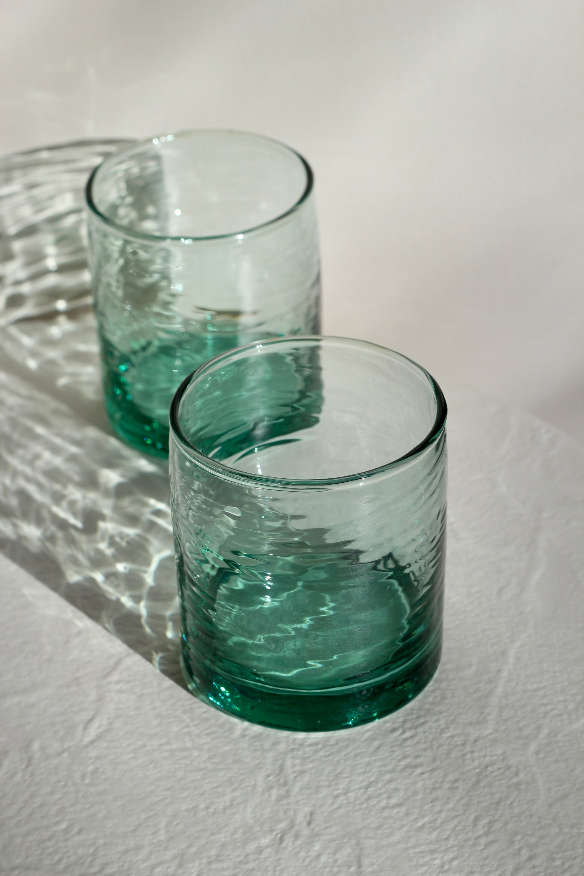 Two wavy green glass tumblers on a textured white surface