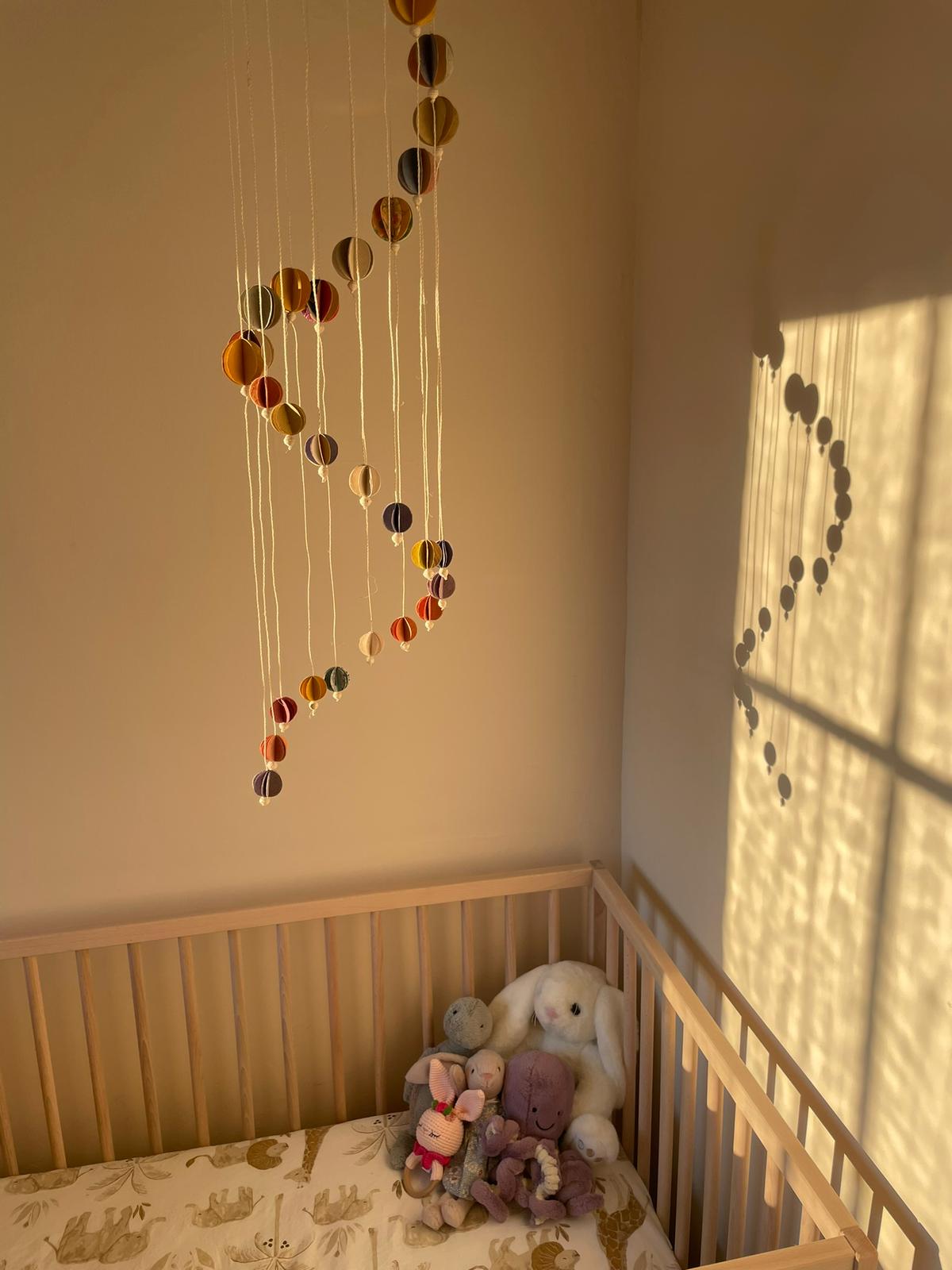 A colorful handmade baby mobile with origami-style paper planets hanging over a crib in a nursery room.