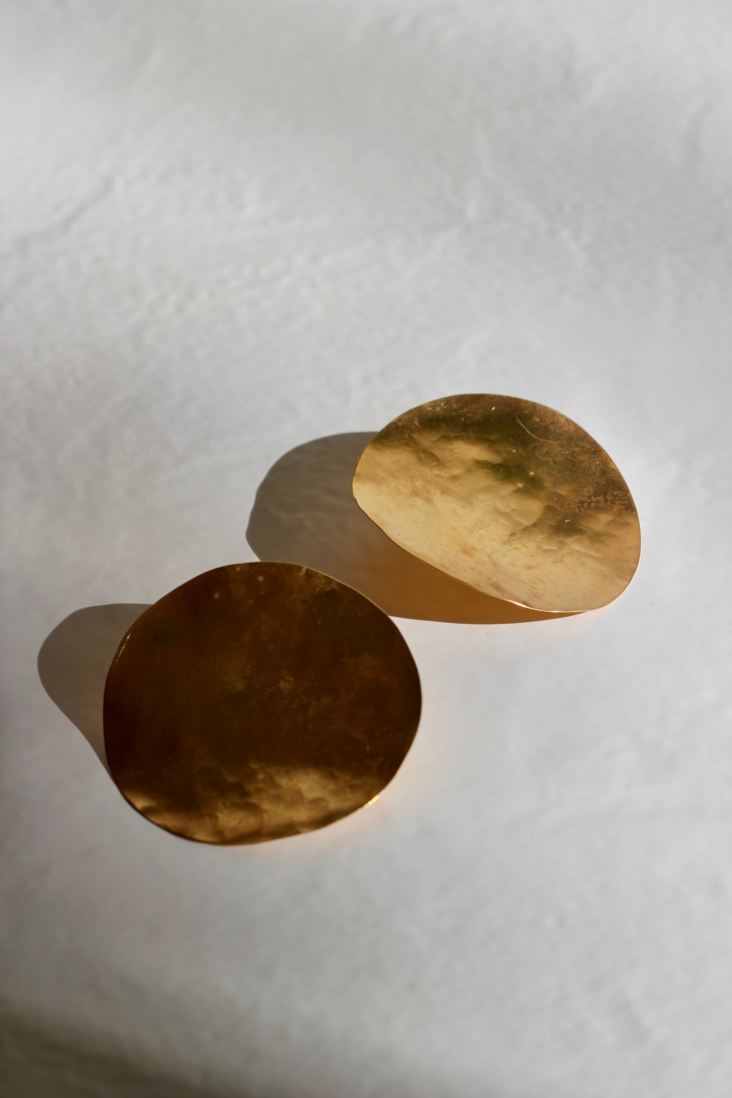 Two handmade gold disc earrings on a white background