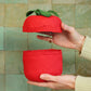Red woven tomato basket held by a hand against a tiled wall.