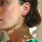 Close-up of a person wearing hand hammered gold hoop earrings with a blurred background