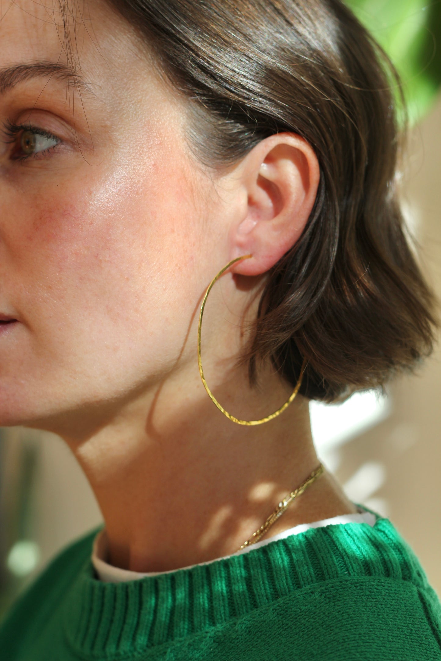 Close-up of a person wearing hand hammered gold hoop earrings with a blurred background