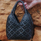 Mini handwoven cuatro tetas bag in black next to a rock wall