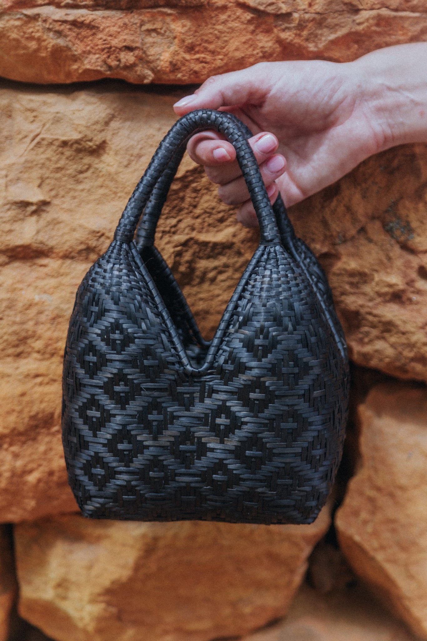 Mini handwoven cuatro tetas bag in black next to a rock wall