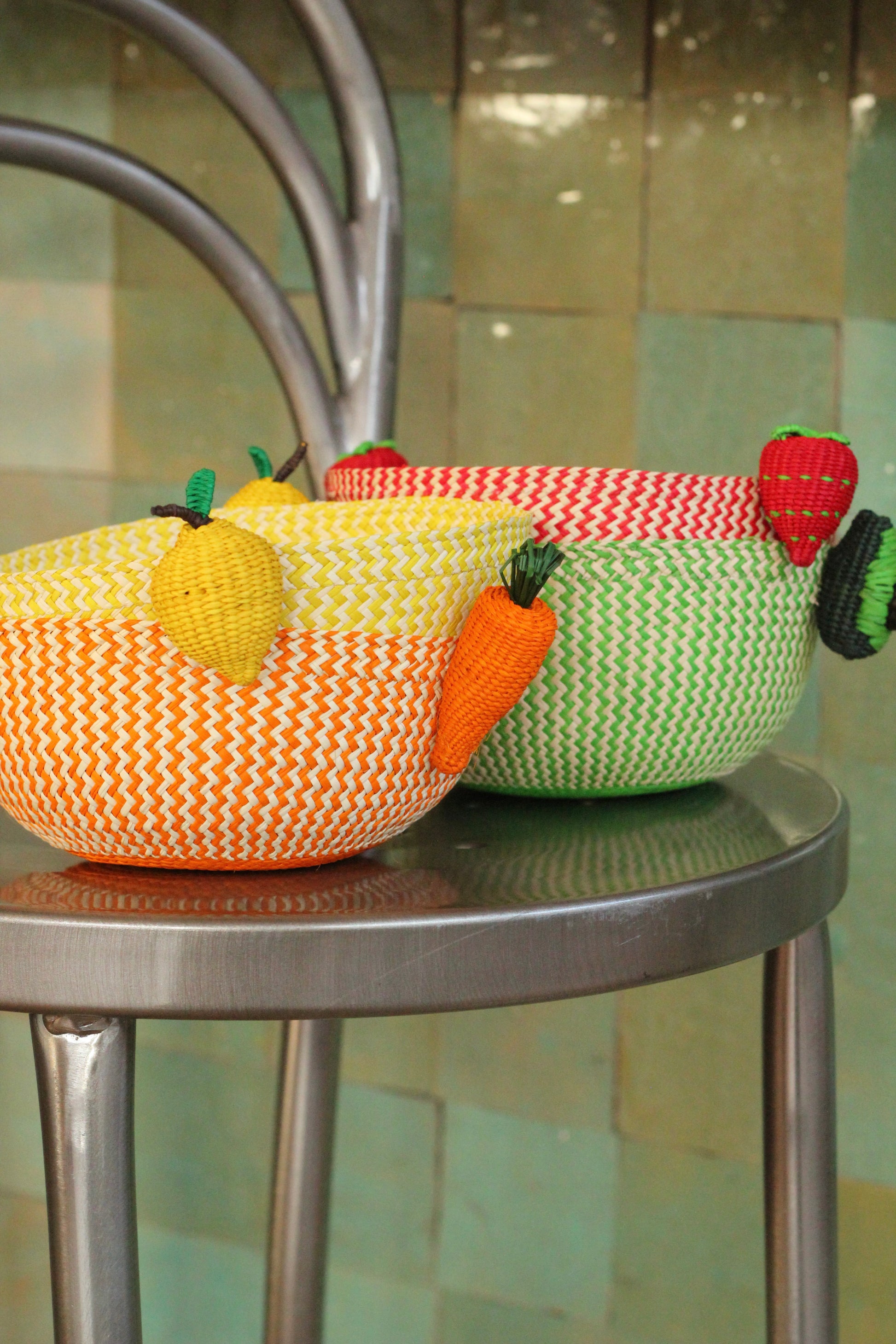 Three colorful mini woven fruit bowls on a metal stool.