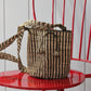 Woven handbag from natural fibers with a striped pattern on a red chair against a white wall.
