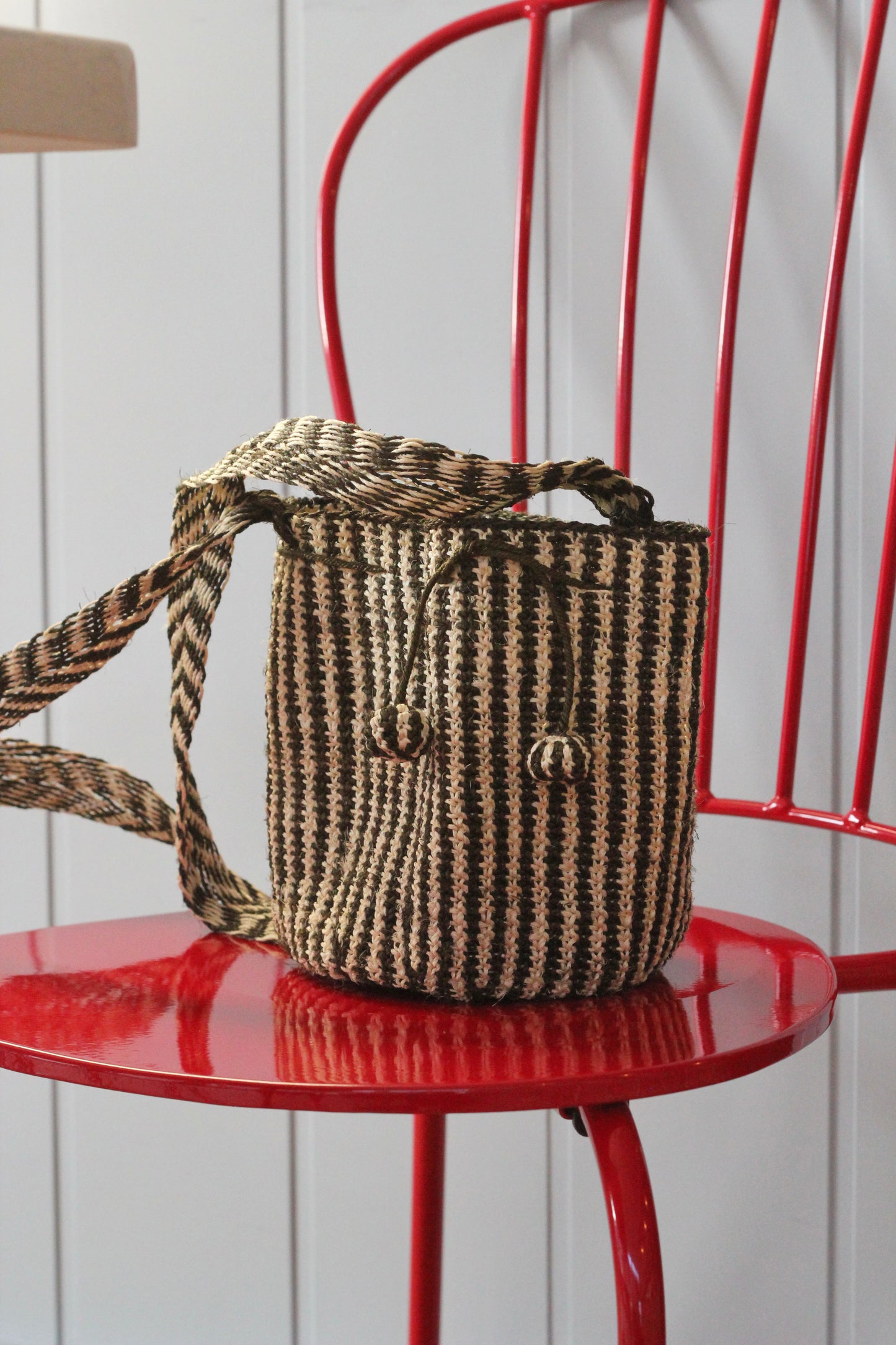 Woven handbag from natural fibers with a striped pattern on a red chair against a white wall.