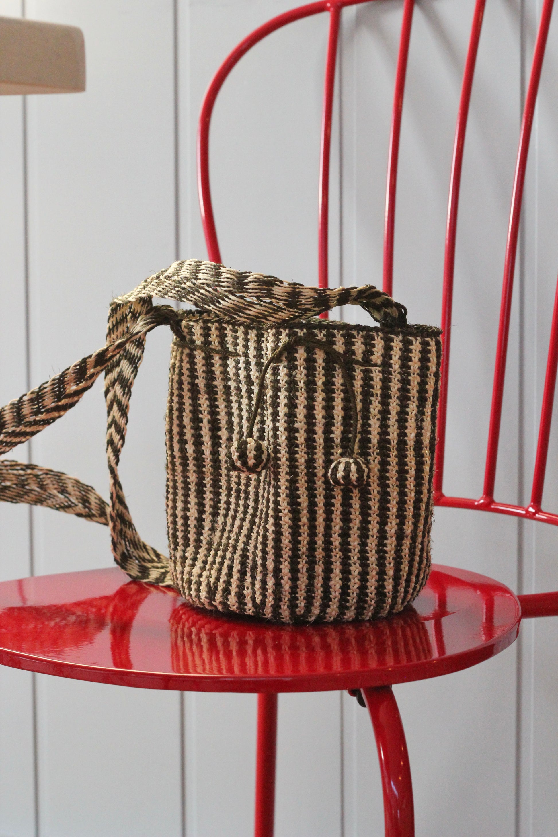 Woven handbag from natural fibers with a striped pattern on a red chair against a white wall.