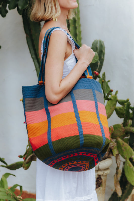 Woman holding a colorful striped oversized tote bag with a cactus background