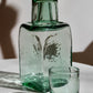 Green handblown recycled glass carafe and glass on a white surface with shadows.