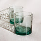 Two green handblown glass tumblers on a white surface