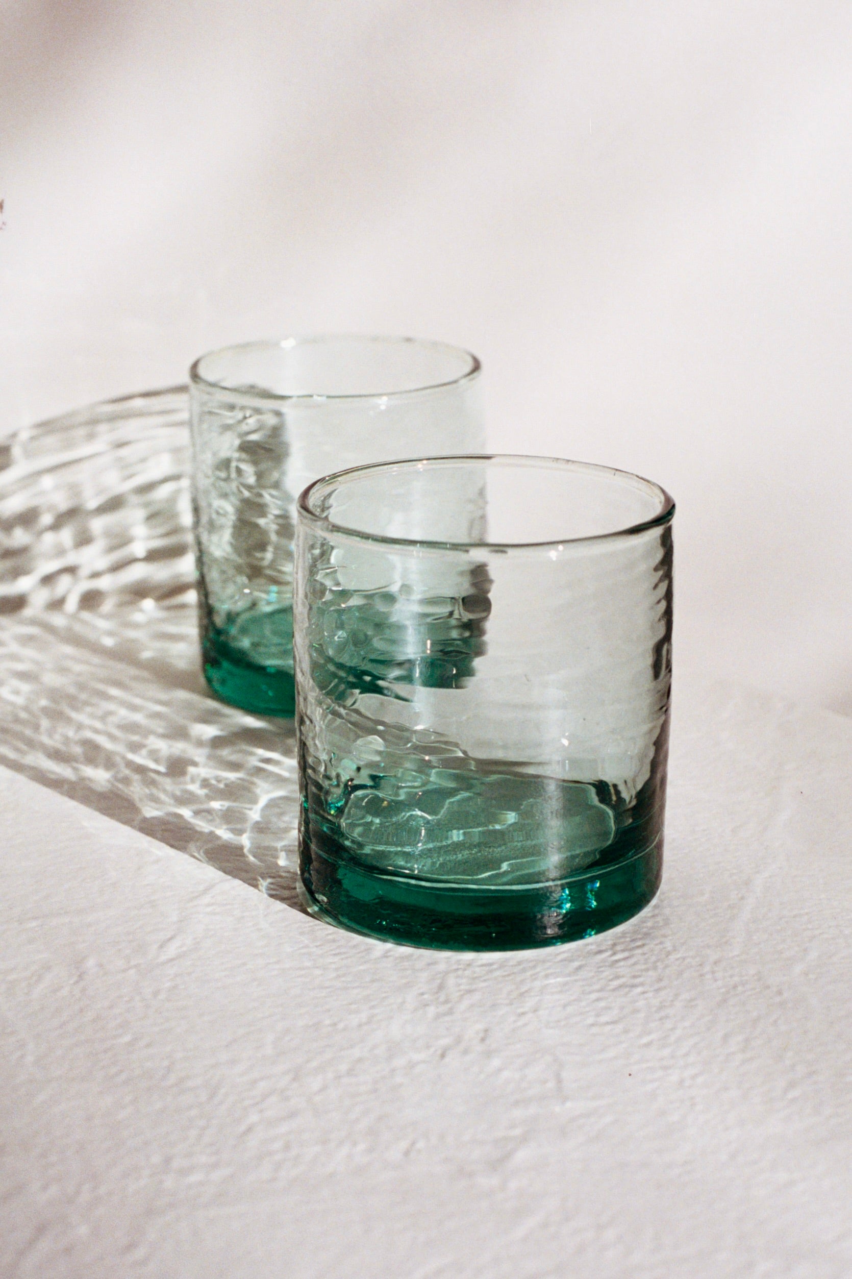Two green handblown glass tumblers on a white surface