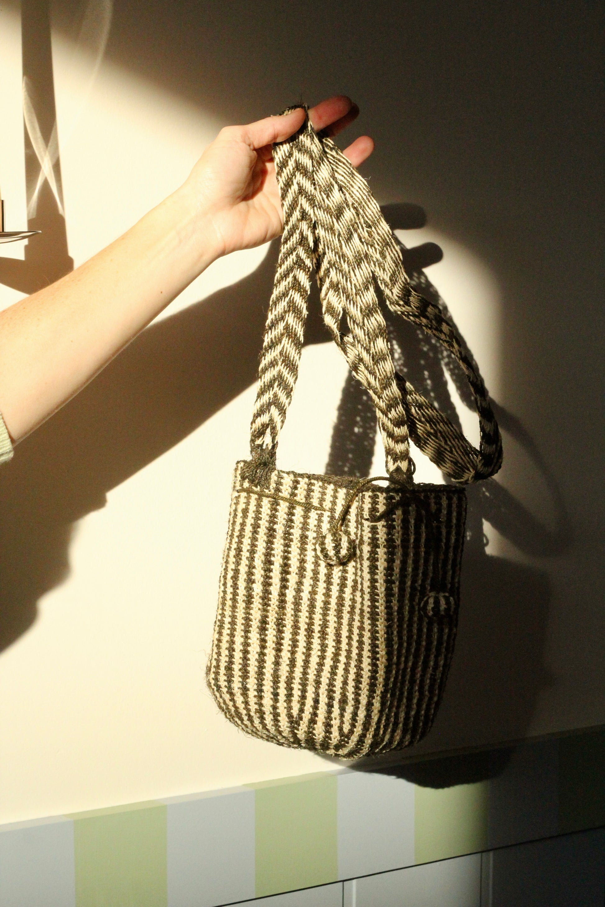 Hand holding a striped handwoven bag against a neutral background