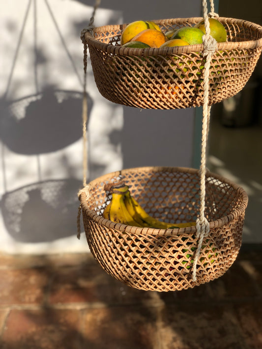Two-tier hanging handwoven baskets made of natural fibers displayed outdoors with fruits inside, likely handcrafted from materials sourced from the Amazon rainforest.