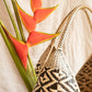 Cuatro tetas handwoven basket with geometric patterns, predominantly black and natural colors, displayed against a backdrop of a potted plant with vibrant orange flowers.