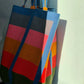 An oversized handwoven tote bag with multicolored stripes in red, blue, green, and yellow, with a black base and colorful straps.