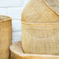 A set of natural, handwoven baskets of varying sizes made from a natural vine fiber, displayed stacked together.